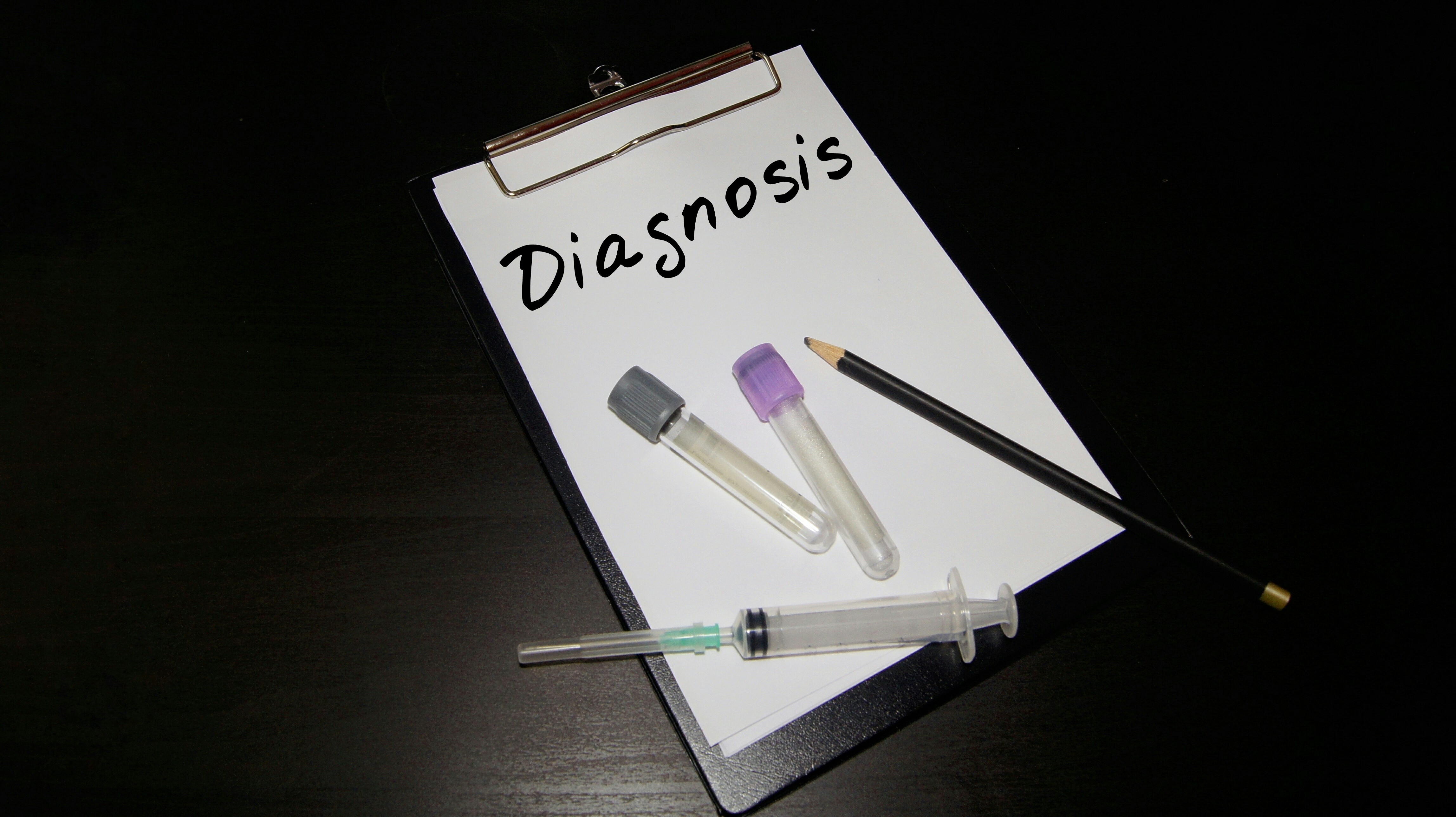 A clipboard with Diagnosis written on it, two blood sample phials, a syringe and a pencil